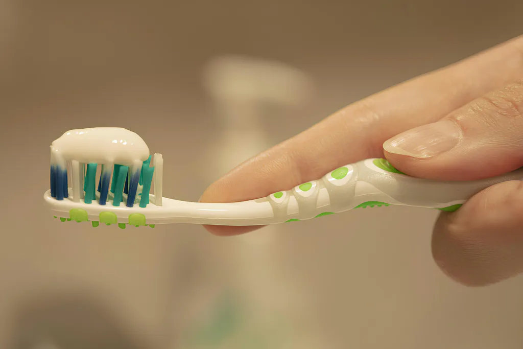 A hand holding a toothbrush with a fresh line of toothpaste