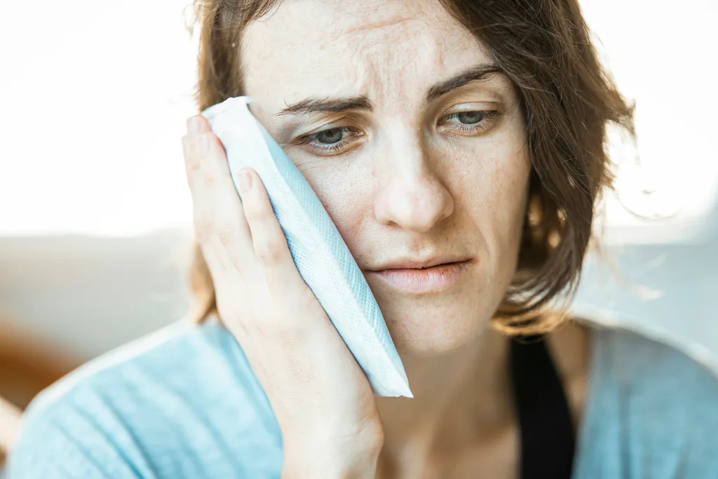 A woman holding a cool cloth to her cheek