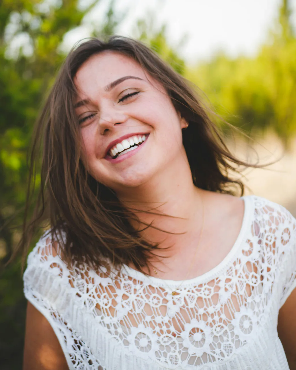 A woman laughing outdoors with a bright, natural smile