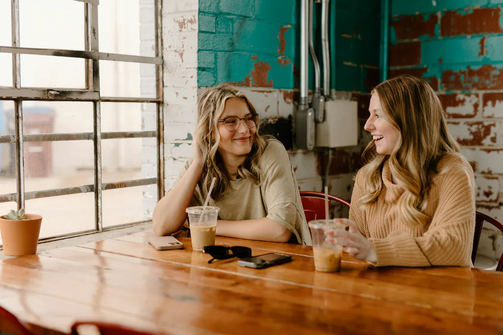 Two women chatting over drinks at a wooden table
