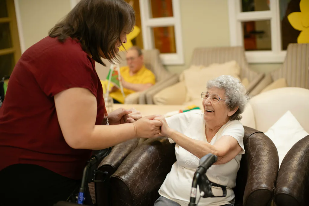 A caregiver helping an older woman in a bright living room