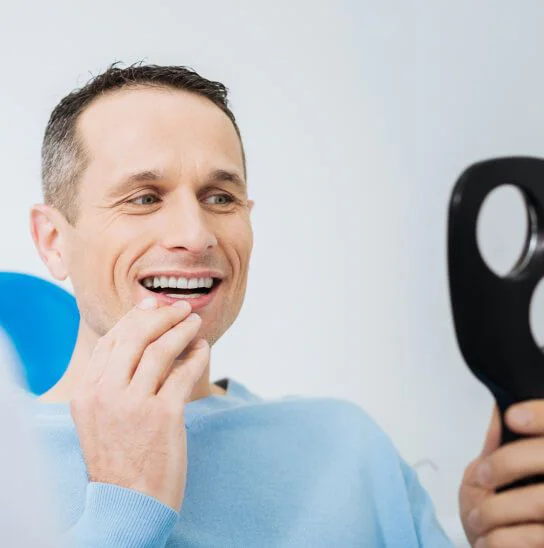 A smiling patient checking his teeth in a hand mirror