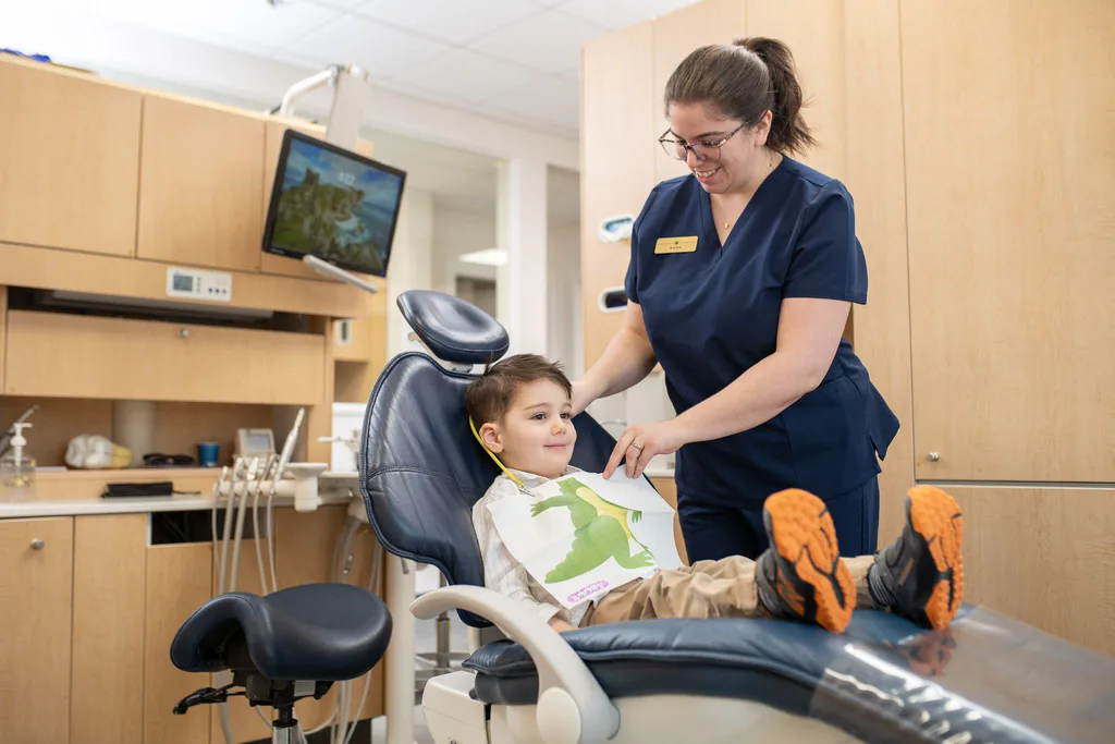 An assistant fitting a bib for a young patient in the chair