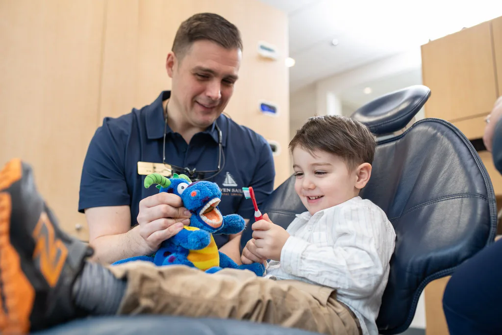 Dr. Séguin showing a delighted young patient how to brush using a plush dragon