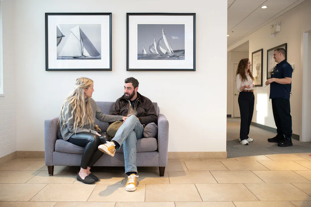 Two patients relaxing in the light-filled lounge beneath framed sailing photographs