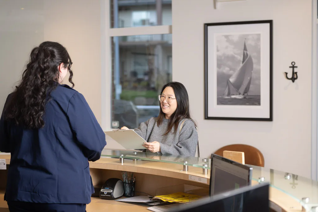 A new patient smiling at the reception desk as she completes her paperwork