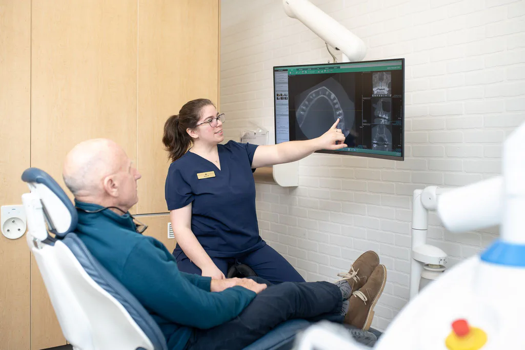 A hygienist showing a patient his digital scan on a large screen