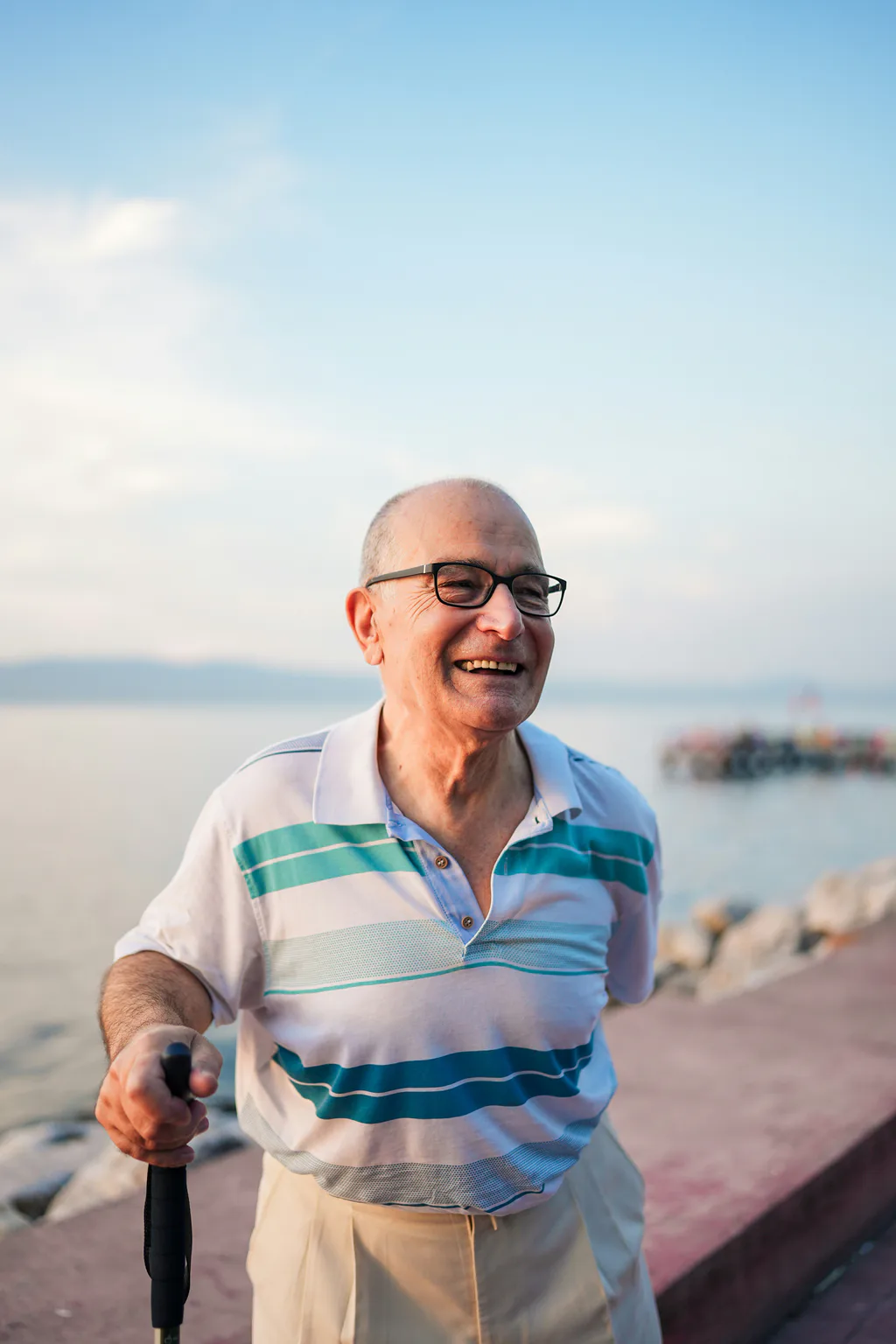 An older man smiling broadly on a sunny seaside promenade