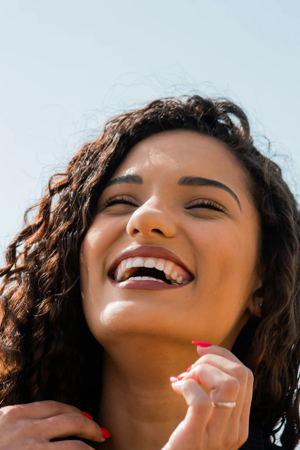 A young woman laughing in the sunshine, showing a bright, natural smile